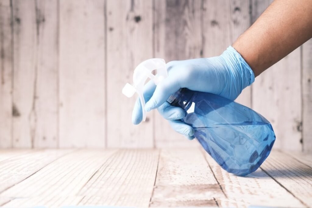 A hand spraying a cleaning mixture on an old wooden surface