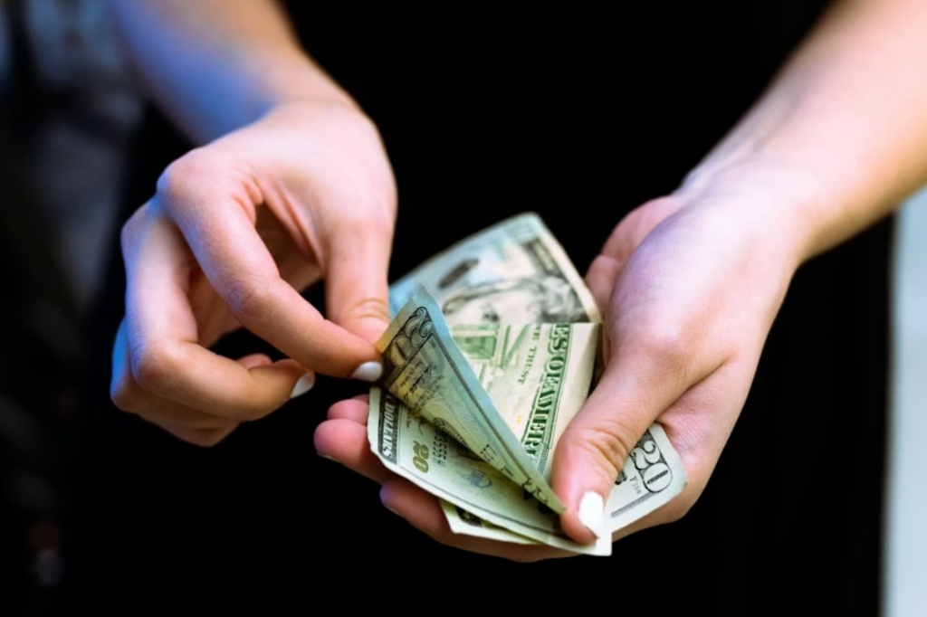 A person in a black shirt is counting $100 bills.