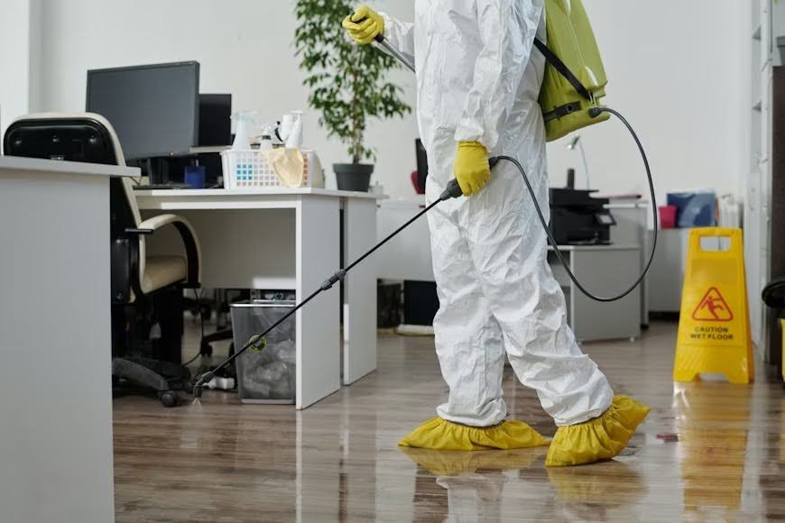 Young male pest control professional in protective workwear, spraying an office floor.